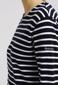 Marineblå og hvid stribet sweater med rund hals, der har en blød tekstur og ordet "Armorux" broderet på ærmet.