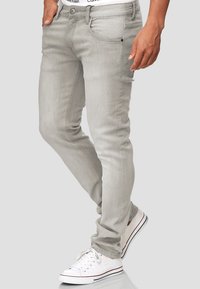 Lichtgrijze jeans hebben een slim fit, een klassiek vijf-pocketontwerp en subtiele stiksels. Gecombineerd met witte sneakers en een zichtbare merk tailleband.