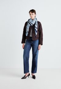 Smeđa kviltana jakna s gumbima, plavi šal s uzorkom, sivi top i tamnoplave ravne traperice, u paru s tamnim cipelama s petom.