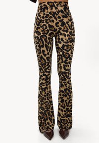 Pantalones de campana con estampado de leopardo de cintura alta en beige y negro, con una textura suave y tela lisa, combinados con zapatos marrones de punta.
