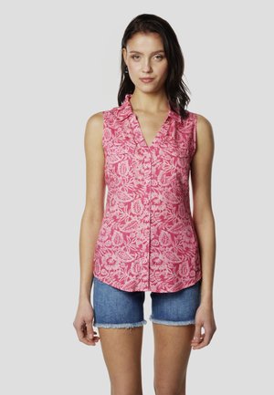 Blusa rosa sin mangas con un patrón floral, botones en el frente y escote en V, combinada con pantalones cortos de mezclilla con bordes deshilachados.