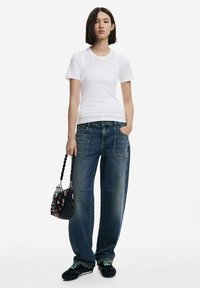 T-shirt bianco aderente, jeans boyfriend blu in denim a vita alta, scarpe nere con accenti colorati e una borsa nera testurizzata con un motivo multicolore.