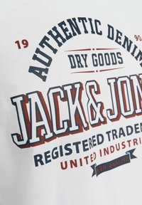 Hvid bomulds t-shirt med fed, flerfarvet tekst: "JACK & JONES," "AUTHENTIC DENIM" og yderligere detaljer i marineblå og bordeaux.