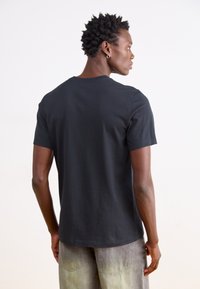 Juodas medvilninis trumpomis rankovėmis T-shirt su klasikiniais apvaliais iškirpimu, išsiskiriantis lygiu paviršiumi ir tiesiu kirpimu, pateiktas iš nugaros.