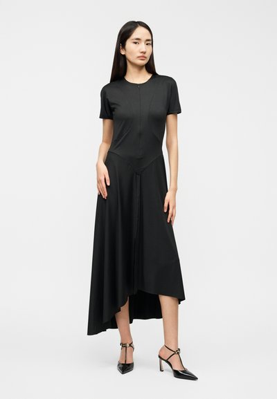 Μαύρο φόρεμα με κοντά μανίκια, ασύμμετρο τελείωμα, εφαρμοστό μπούστο και κλείσιμο με φερμουάρ. Το μοντέλο το συνδύασε με μαύρες γόβες, τονίζοντας τον κομψό σχεδιασμό.