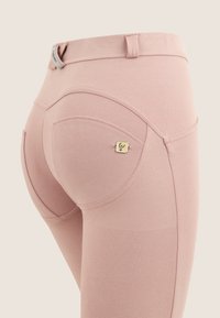 Leggings rosa realizzati in tessuto elastico, con vita media, cuciture curve e un piccolo logo sulla tasca posteriore.