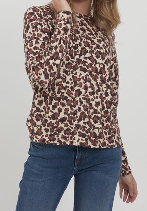 Top à manches longues en imprimé léopard crème, avec des taches noires et bordeaux. Tissu doux avec une coupe décontractée et un col arrondi. Jean en denim visible.