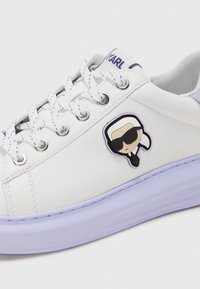 Witte leren sneaker met paarse accenten, voorzien van gemarmerde veters en een cartoonlogo van een figuur met een zonnebril aan de zijkant.