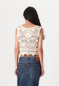 Häkel-Top in Off-White mit kreisförmigen Mustern und gewellten Kanten. Kombiniert mit einem hoch taillierten Jeansrock mit Lederpatch.