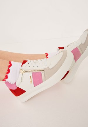 Noge, obute v bele superge z rožnatimi, bež in rdečimi paneli, z zlatim zadrgo in belimi nogavicami z rdečimi nazobčanimi robovi.