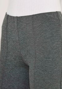 Close-up van het midden van het lichaam met grijs textuur broek en een witte geribbelde trui.