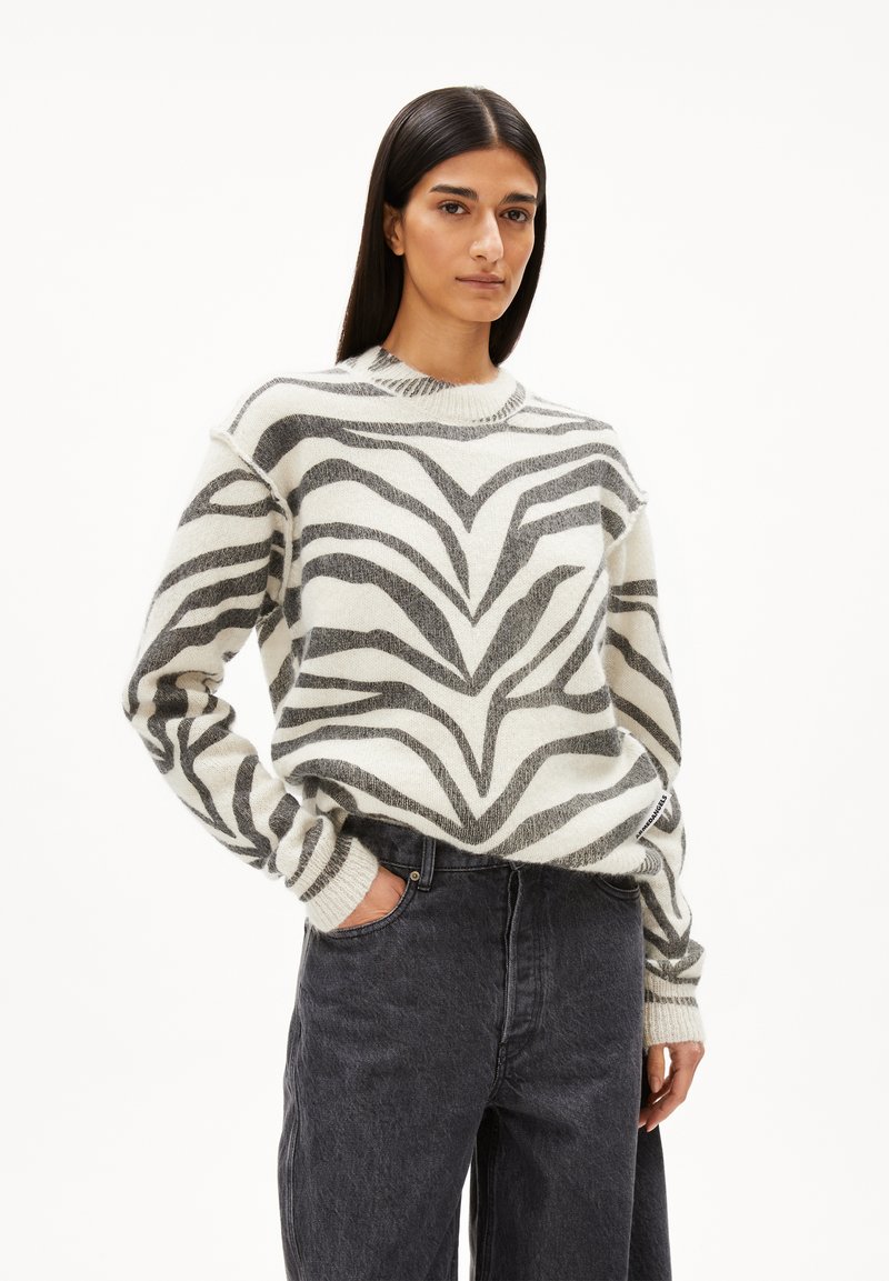 Pull en mélange de laine avec un motif zèbre noir et crème, col rond et poignets côtelés. Associé à un jean en denim foncé taille haute.
