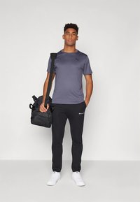 Sivo atletsko majico z logotipom, črne hlače za tek z belim logotipom, beli supergi in črni nahrbtnik. Enostavna, športno priložnostna obleka.