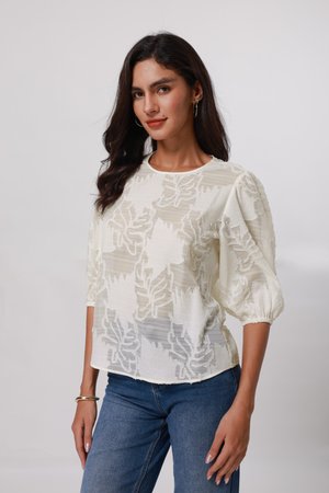 Weiße bestickte Bluse mit einem strukturierten Blattmuster, rundem Ausschnitt und Puffärmeln, kombiniert mit blauen Jeans. Leichtes, luftiges Material.