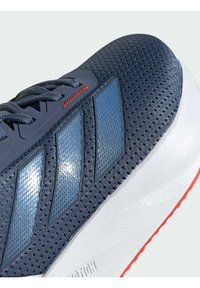 Scarpa sportiva in mesh blu con tre strisce textured blu, dettagli riflettenti, lacci piatti e una suola imbottita bianca e rossa.