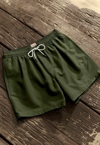 Zöld fürdőnadrág, rugalmas derékkal, fehér zsinórral és barna részletekkel, könnyű, sima anyagból készült.