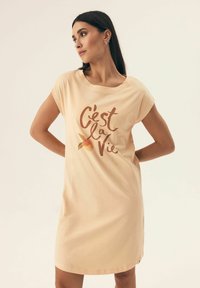 Różowa sukienka z miękkiego materiału z krótkimi rękawami, z nadrukowaną frazą "C'est la Vie" i pomarańczową grafiką.