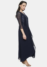 Granatowa sukienka wieczorowa z koronkowym gorsetem obleczonym cekinami i rękawami o długości trzy czwarte, z lekko spływającą spódnicą z bocznym drapowaniem.