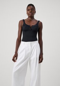 Bodysuit negro con copas estructuradas, tirantes gruesos y un detalle de escote en forma de llave, acompañado de pantalones anchos blancos. Tela suave, diseño minimalista.