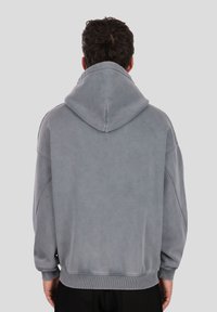 Siva jopa s kapuco z ohlapnim prileganjem, mehko teksturo, rebrastimi manšetami in robom. Ima minimalističen dizajn brez vidne blagovne znamke.