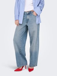 Ljusa blå jeans med breda ben och hög midja, kombinerade med röda spetsiga klackskor. Outfiten kompletteras med en blårandig oversize-skjorta.