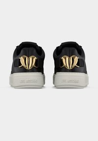 Μαύρα αθλητικά παπούτσια με λευκές σόλες που διαθέτουν διακοσμητικά από χρυσό μέταλλο σε σχήμα καρδιάς και την επιγραφή "Love Moschino" στο τακούνι.