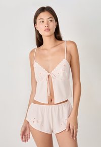 Set da notte rosa chiaro composto da una maglietta corta con un nodo frontale e bordi a scalloped, abbinato a pantaloni corti con dettagli di ricamo floreale.
