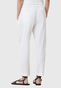 Pantaloni bianchi leggeri con vita elastica e due tasche posteriori. Abbinati a sandali neri con fasce e suola piatta.