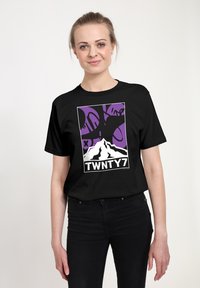 Černé tričko s potiskem hory v bílé barvě, na fialovém pozadí s abstraktními černými tvary. Text zní "TWNTY7." Krátké rukávy a standardní střih.