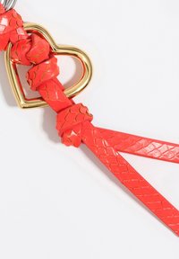 Czerwone plecione paski z sercowym złotym metalowym akcentem. Skóra ma teksturowany wzór w skale, co zwiększa atrakcyjność wizualną projektu.