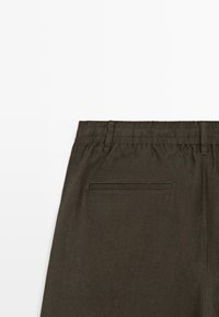 Bukser med mørkeolivengrøn elastisk talje, bæltestropper og en enkelt baglomme med kantsøm, vist bagfra.