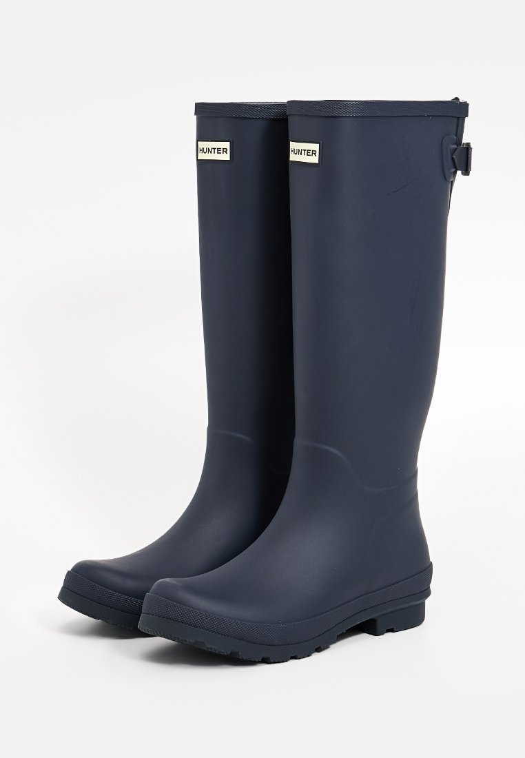Waterdichte rubber laarzen tot de knie in marineblauw, met een gestructureerde zool, verstelbare riem en een merklabel aan de voorkant.