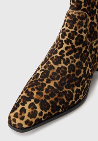 Bottines à imprimé léopard avec un bout pointu, en matériau texturé semblable à de la fourrure, et une semelle noire lisse, mettant en avant des motifs distincts de marron et de noir.