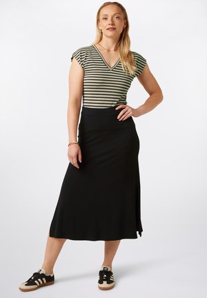 Czarna spódnica do kostek w połączeniu z bluzką w paski z dekoltem w serek w kolorach ciemnej zieleni, kremowego i fioletowego. Modelka ma na sobie czarno-kremowe sneakersy.