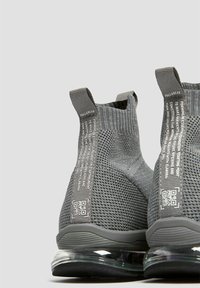 Szare, dziane sneakersy za kostkę z teksturowanym wzorem, uchwytami do zakupu, akcentami w postaci kodu QR oraz przezroczystą, powietrzną podeszwą.