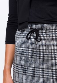 Haut noir à manches longues au-dessus d'un pantalon à carreaux taille haute, pull-on en noir et blanc, avec un cordon de serrage et des accessoires en argent.