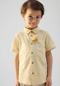 Korte mouwen geel shirt met bloemenborduursel, knoopsluiting aan de voorkant en een borstzak. Heeft een bloemenaccent vastgepind aan de kraag.