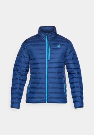 Chaqueta azul acolchada con alto cuello, presenta un cierre frontal y acentos en un azul claro contrastante. Incluye un logo de araña en el pecho.