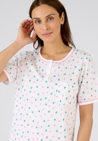 Camisa blanca de manga corta con cuello redondo, que presenta patrones de corazones coloridos en rosa y verde, y un bolsillo en el lado izquierdo del pecho.