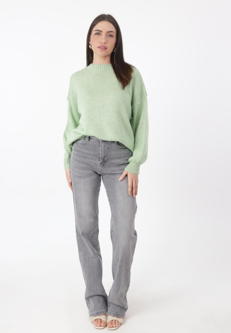 Hellgrüner gestrickter Pullover mit einem gerippten Ausschnitt, kombiniert mit grauen, geraden Jeans und hellen Sandalen. Schlichtes Design, weicher Stoff.