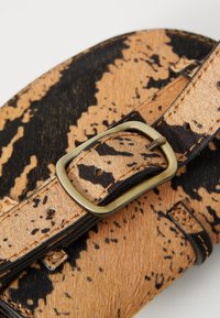 Borsa a spalla in pelliccia sintetica maculata marrone e nera, con fibbia in metallo tono oro, tracolla piatta e dettagli cuciti.