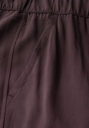 Gros plan sur un tissu bordeaux mettant en avant une texture lisse, une taille élastique et des détails de poches sur les côtés. Les coutures présentent des surpiqûres discrètes.