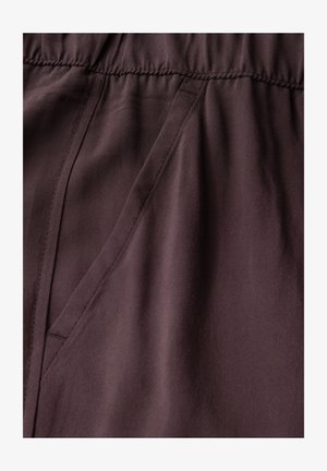 Burgundowa tkanina zbliżenie, charakteryzująca się gładką fakturą, elastycznym pasem i detalami bocznej kieszeni. Szwy z subtelnym przeszyciem.