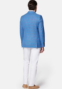 Niebieska marynarka w kratę z teksturowanej tkaniny, w połączeniu z białymi spodniami i jasnobrązowymi loafersami, widziana z tyłu.