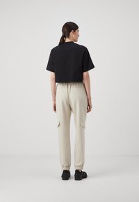 Kuttet svart t-skjorte med korte ermer, sammen med kremfargede joggebukser med sidelommer og elastiske mansjetter, iført svarte treningssko.