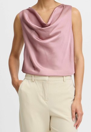 Różowa, bezrękawnikowa bluzka z satyny o zmierzchowym odcieniu i drapowanym dekoltem, zestawiona z beżowymi spodniami z wysokim stanem, ręce w kieszeniach, na osobie.