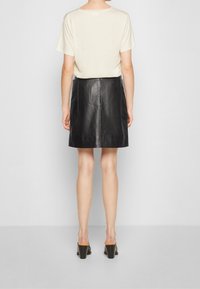 Svart läder minikjol med sidofickor, kombinerad med en ljusbeige kortärmad topp. Enkel design och slät yta, vy från baksidan.