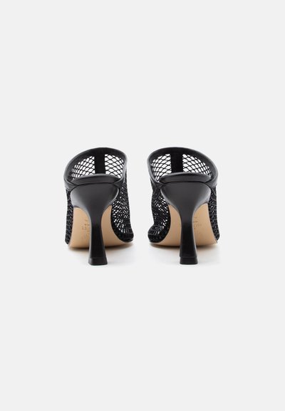Ζευγάρι μαύρα διχτυωτά μιούλ με ψηλές μυτερές στιλέτο φτέρνες, εμφανιζόμενα από πίσω σε λευκό φόντο.