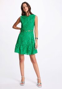 Robe sans manches verte avec un motif floral découpé au laser et une jupe évasée. Présente un col rond et un subtil bord festonné.