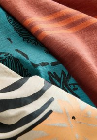 Tre vikta tyger i olika färger: rostfärgad med ränder, teal med svarta mönster, och creamfärgad med svart/zebra och orange motiv.